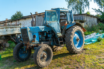 Fototapeta premium An old rusty Soviet-era tractor is parked on a farm plot. Repair of agricultural machinery. Poor regions of Russia. Lack of financing of private farms.