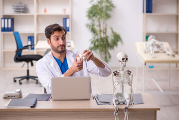 Young male doctor studying human skeleton at the hospital