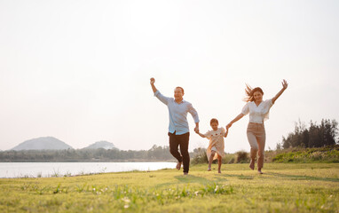 Fototapeta na wymiar Happy family in the park sunset light. family on weekend running together in the meadow with river Parents hold the child hands.health life insurance plan concept.