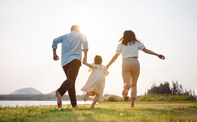 Happy family in the park sunset light. family on weekend running together in the meadow with river...
