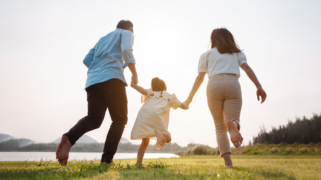 Happy family in the park sunset light. family on weekend running together in the meadow with river Parents hold the child hands.health life insurance plan concept.