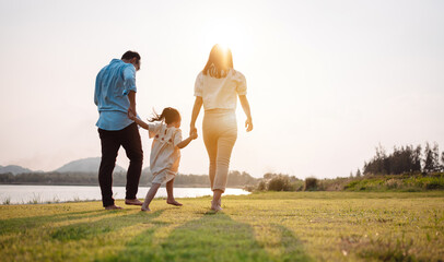 Happy family in the park sunset light. family on weekend running together in the meadow with river...