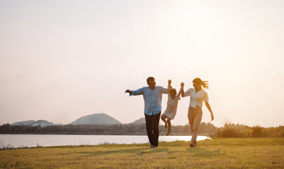 Happy family in the park sunset light. family on weekend running together in the meadow with river Parents hold the child hands.health life insurance plan concept.