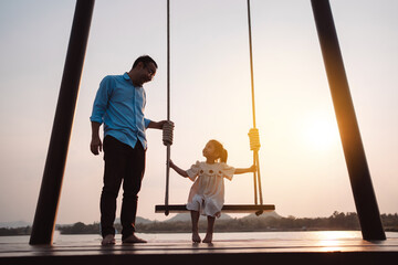 Happy family enjoying with swing in the park at sunset outdoor in nature, Weekend activity of family life together.