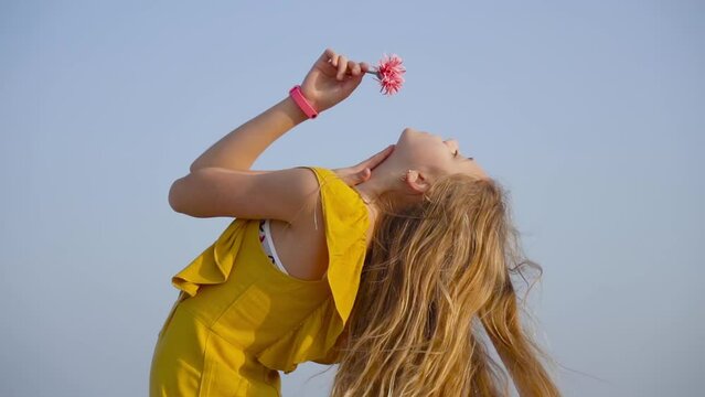 Teen bends over with a flower in her hand in slow motion