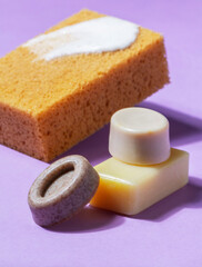 Handmade soap with the addition of coffee and wild herbs and a sponge with foam on a purple background.