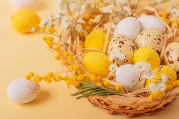 Obraz premium Easter candy chocolate eggs and almond sweets lying in a bird's nest decorated with flowers and feathers on a yellow background. Close up. Happy Easter concept.