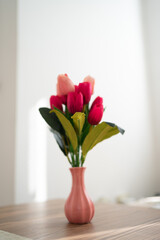 Close up photo of woman's hand holding a pink tulips in vase, flower decoration in home.