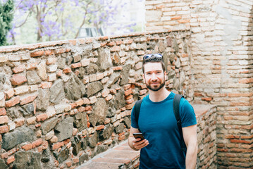 Young man traveller with a beard on a background of an old brick wall of a town in Spain.