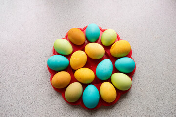 Bright Easter eggs lie on a red, round stand on a marble table. Homogeneous lifestyle background.