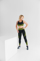 Plakat an attractive blonde in a black and green tracksuit poses on a white background.