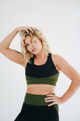 an attractive blonde in a black and green tracksuit poses on a white background.