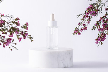 Obraz na płótnie Canvas Skin care serum in transparent glass bottle with dropper on white marble podium on white background with small purple flowers. Skin care concept. Natural organic cosmetic products.
