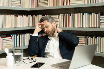 Fototapeta premium Millennial Businessman in office having headache. Business man in suit work on laptop at home office take off glasses suffer from migraine or headache. Tired exhausted man suffering from headache.