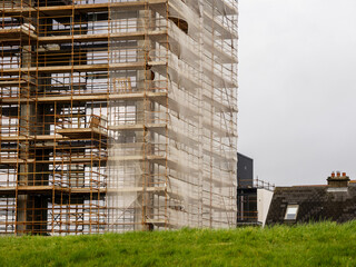 Side of a new building in scaffolding and safety nets. Construction site safety measures. Developing commercial or residential property. Growth concept.