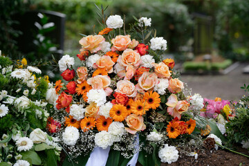 stylish funeral flowers of white carnations, orange gerbera and red and pink roses on a grave after...