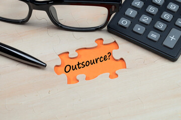 A message on OUTSOURCE on the orange background with a pen, eyeglasses, and calculator at the side. human resource management concept