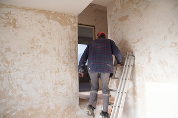 a male builder stands in an apartment near peeling walls and starts repairs