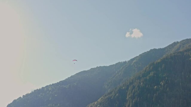 Bright red paraglider flies over large green valley and mountains. Picturesque view, located near the iconic Neuschwanstein castle, Germany, Allg&auml;u region