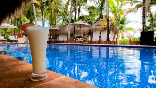 Tropical drink on luxury beach resort tile bar with palm trees and pool in the background