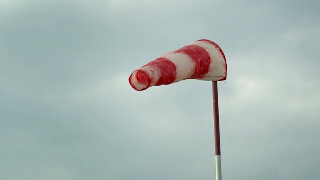 Red and white windsock, wind sock against cloudy sky indicating the forece and direction of the wind on the aerodrome runway