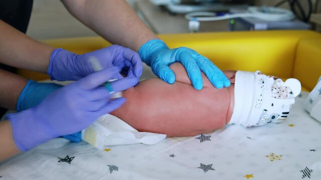 Giving a shot to a little newborn Caucasian baby. Nurse in gloves prepares the syringe and other pair of gloved hands is holding a child. Close up.