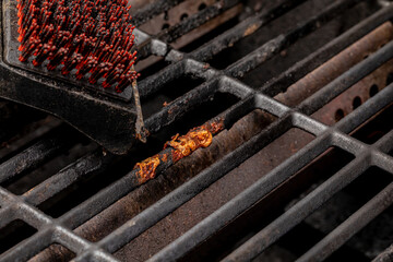 Nylon brush cleaning burnt food stuck on dirty barbecue grill grates. Barbeque grilling, cleaning...