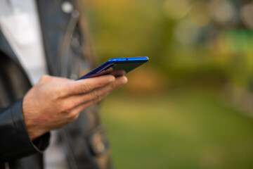 Closeup shot of an young modern man holding mobile phone in hand, blurred background