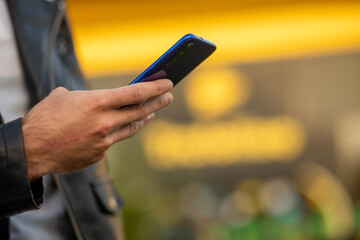 Closeup shot of an unrecognizable man holding mobile phone in hand, blurred yellow background