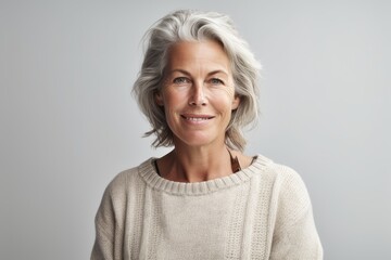 Fototapeta premium Confident mature woman smiling in cozy white sweater on pure neutral grey background. Generative AI