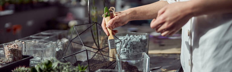 caucasian confident happy florist is working with composition made from glass stones and plants in botanic shop