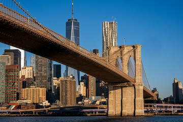 Fototapeta na wymiar Brooklyn, NY - USA - March 26, 2023 Sunrise view of lower Manhattan, featuring the Brooklyn Bridge, World Trade Center, and Frank Gehry’s 8 Spruce Street, seen from across the East River in Brooklyn.