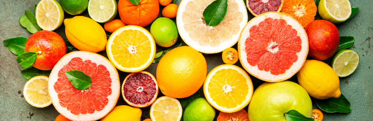 Citrus fruit food background, top view. Mix of different whole and sliced fruits: orange, grapefruit, lime and other with leaves on  green table. Banner
