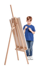 Little boy painting against white background. Using easel to hold canvas