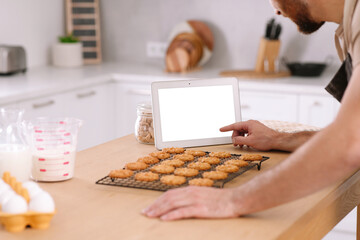 Man with freshly baked cookies watching online cooking course via tablet in kitchen, closeup