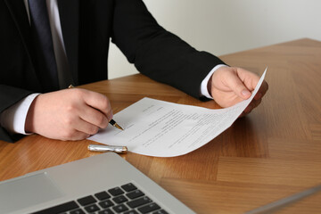 Notary signing document at wooden table, closeup
