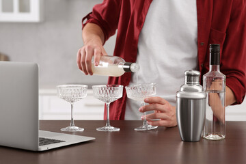 Man learning to make cocktail with online video on laptop at wooden table in kitchen, closeup. Time for hobby