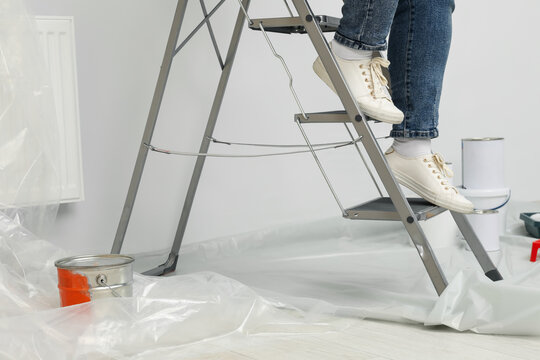 Woman climbing down metallic folding ladder near painting tools indoors, closeup
