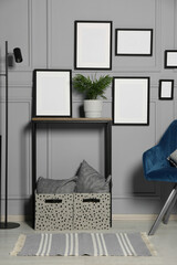 Stylish room interior with empty frames hanging on grey wall near console table