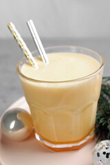 Glass of delicious eggnog and decorated fir branch on gray table, closeup