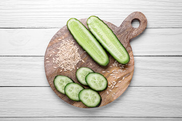 Pile of vegetable seeds and fresh cucumbers on white wooden table, top view