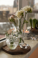 Different beautiful spring flowers and candles on windowsill indoors