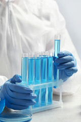 Scientist taking test tube with light blue liquid at white table in laboratory, closeup