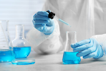 Scientist dripping liquid from pipette into beaker at white table in laboratory, closeup