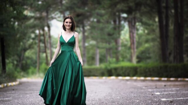 Beautiful young woman in luxury silk satin green dress with long waving train walking towards the camera. Prom dresses shooting , selective focus