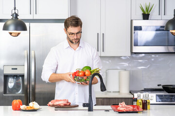 Handsome man cooking salad in kitchen. Guy cooking on kitchen with vegetables. Portrait of casual man cooking in the kitchen with vegetable ingredients. Casual man cooking salad at home in kitchen.