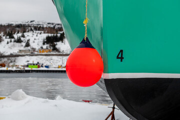 A vibrant green fishing boat on dry dock with a white and black strip on the bow. There is a number four on the green paint indicating a four-meter waterline. An orange rubber buoy hangs from the bow. - obrazy, fototapety, plakaty