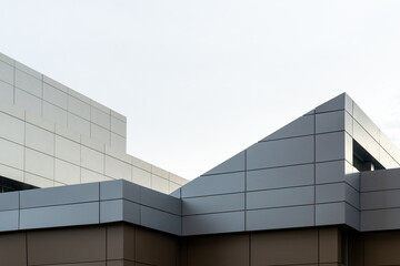 Commercial external metal composite panels on a building with blue sky and clouds in the background. The durable metal composite panels are two shades of grey in color on the modern building.