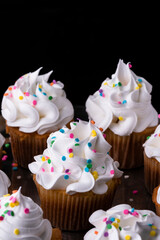Fluffy vanilla cupcakes, with meringue and dragees on a black background.