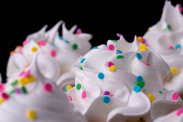 Fluffy vanilla cupcakes, with meringue and dragees on a black background.